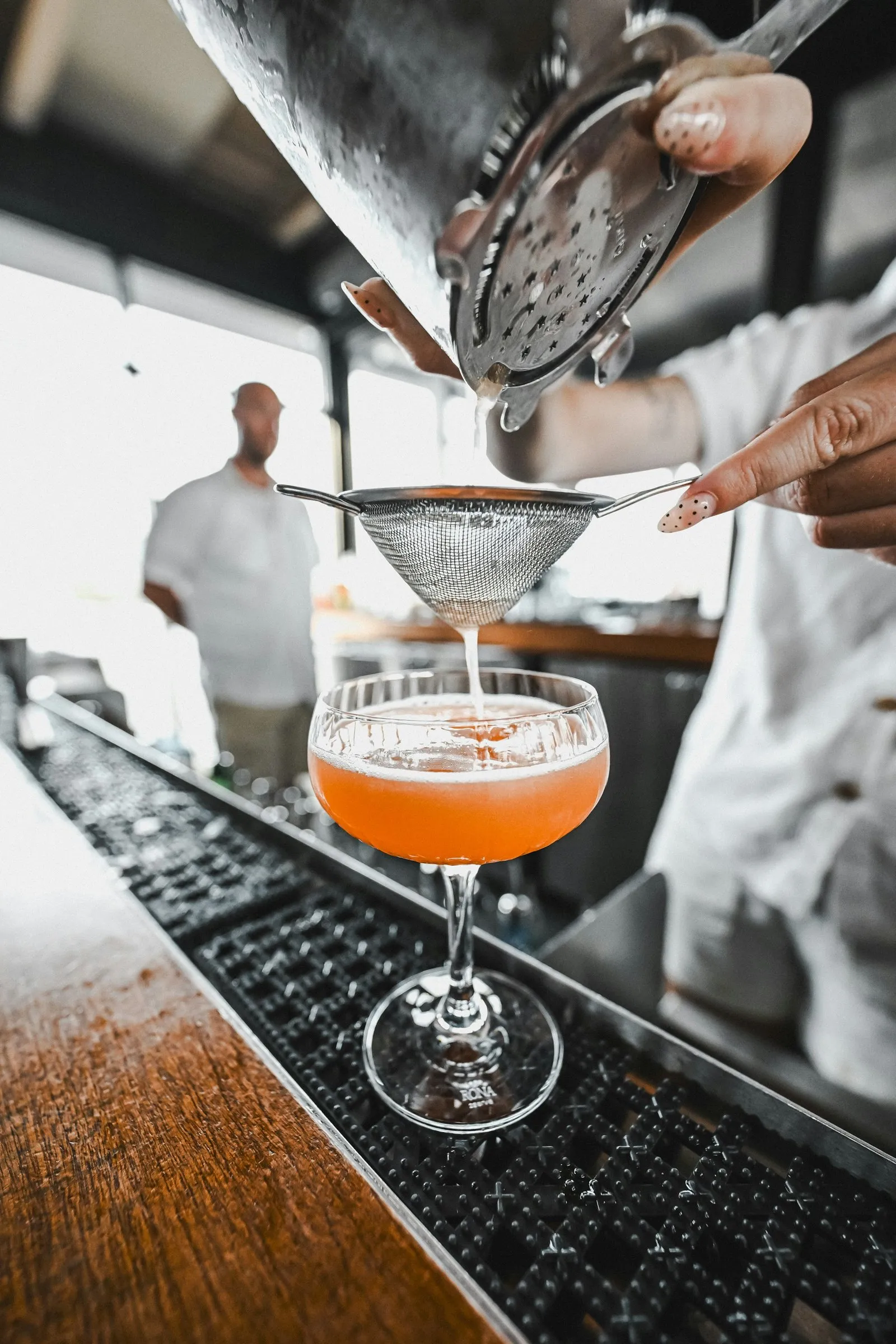 A bartender straining an orange cocktail into a coupe glass